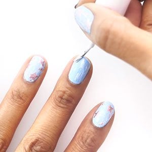 Empieza tu diseño de uñas con estrellas aplicando una base de essie y sigue con una capa de esmalte azul y otra de esmalte blanco. 