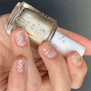 Esta idea de uñas navideñas elegantes te va a encantar. Fondo de la uña desnudo, con solo brillo, y unos minidetalles dorados que puedes trabajar perfectamente con el esmlte Penny Talk de essie. ¿Te gusta?