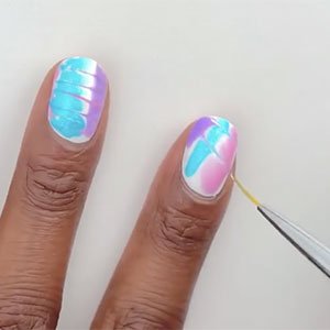 Tu manicura tie-dye requiere mucha velocidad. Una vez hayas aplicado los tres trazos de color con los esmaltes Lovie Dovie, Bikini so teeny y Lilacism de essie, tendrás que atravesarlos con unas líneas diagonales para las cuales necesitarás utilizar un pincel fino.