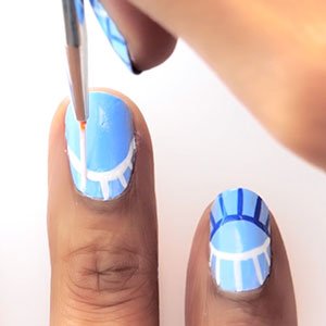 Pinta tus uñas con ojos mojando un pincel preciso en el esmalte Blanc de essie y después en otro de color azul oscuro. 