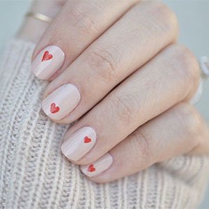 Las uñas color piel también pueden incorporar motivos artísticos como estos corazones. Replica esta manicura con la ayuda de los esmaltes Not just a pretty face y Really Red de essie.